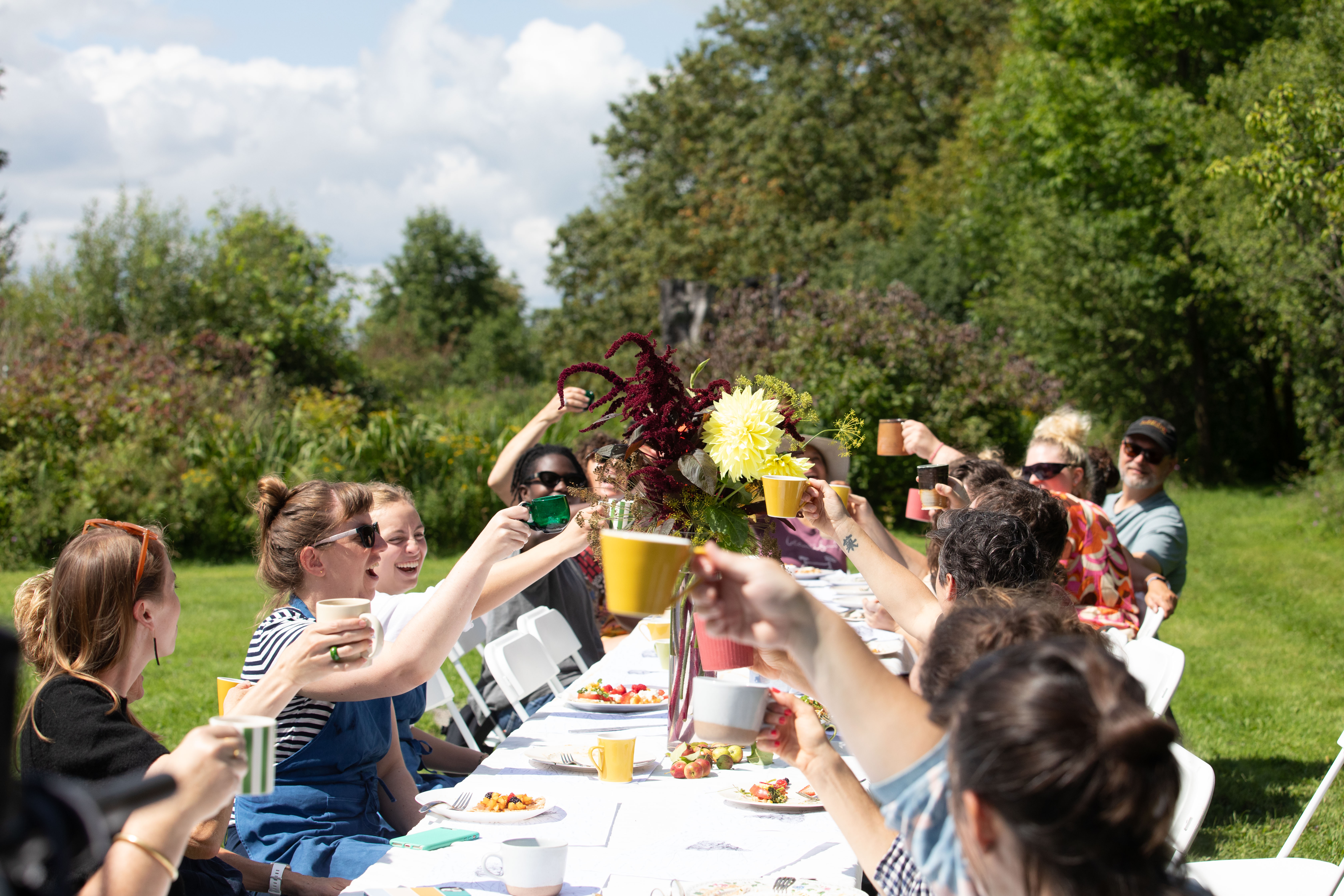 A group of people sitting around a dining table outside, raising their drinks in a toast